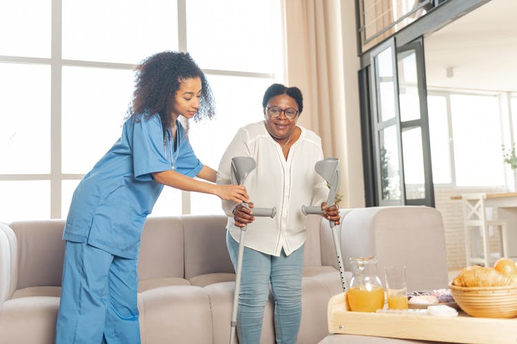 home health nurse helping stroke patient stand up from couch using cane to avoid falls
