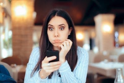 frau mit schockiertem ausdruck, die auf ihr telefon schaut
